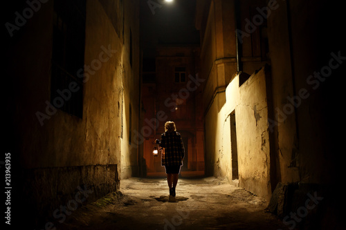 Mysterious blonde woman in elegant retro coat with old oil lantern walking in old French street in Paris, noire atmosphere, investigating crime, detective concept