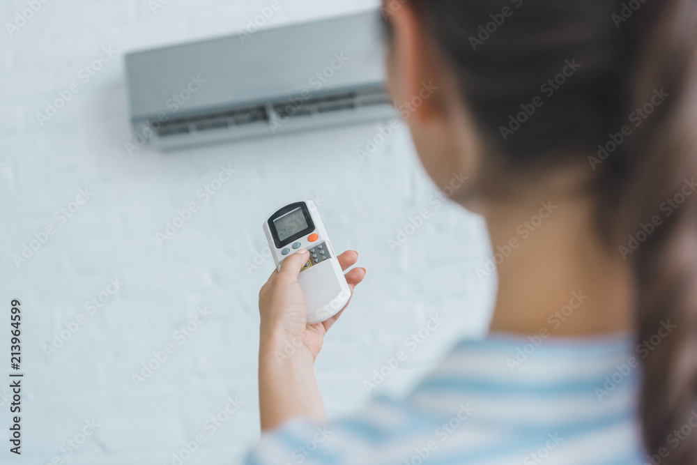 selective focus of woman turning on air conditioner with remote control selective focus of woman turning on air conditioner with remote control