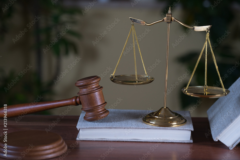 Lawyers office room with the scales of justice, hammer and old law books in the background Lawyers office room with the scales of justice, hammer and old law books in the background