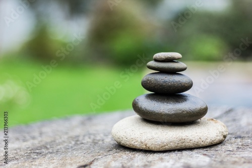 Canvas Print Black and grey zen stones in equilibrium on right side of wooden platform with green background