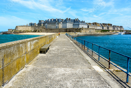 General view of the walled city of Saint-Malo in Brittany, France, with the granite residential buildings sticking out above the rampart, seen from the breakwater under a summer blue sky.