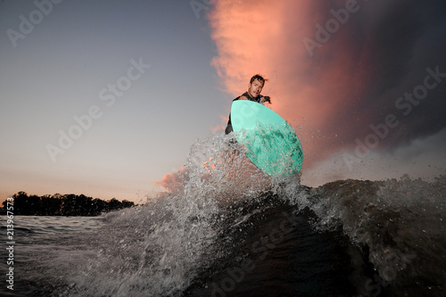 Young wakesurfer riding down the river waves at the sunset