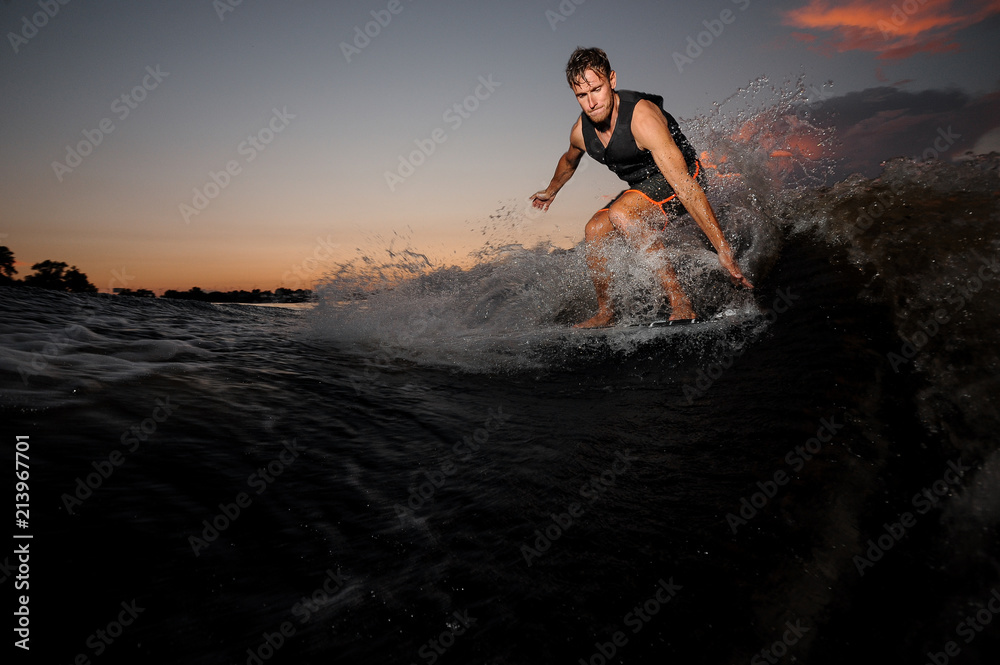 Active wakesurfer jumping on board riding down the river waves at the sunset