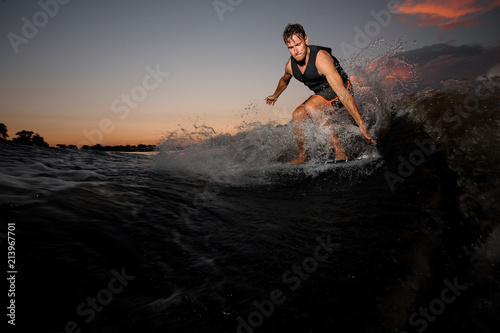 Active wakesurfer jumping on board riding down the river waves at the sunset