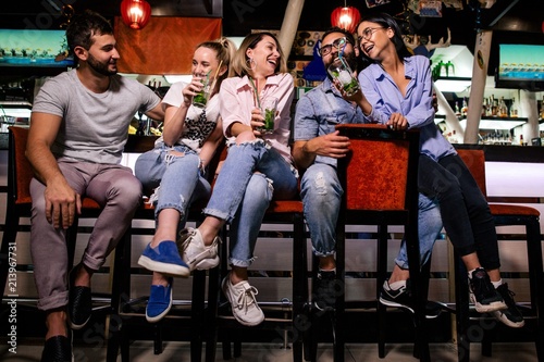Five cheerful friends sit at the bar talking and laughing with each other