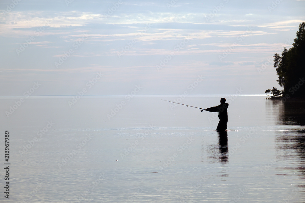 Silhouette of a fisherman at sunset. Fishing on the lake.