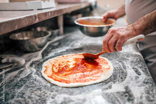 Raw pizza, preparation in traditional style. Adding tomato sauce on a pizza d...
