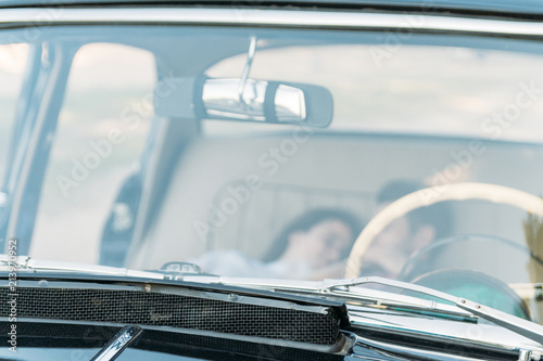 date in the car.people who are lying in the car and holding hands, kissing. look through the window in the car.View from the windshield of the black auto through the white steering wheel.