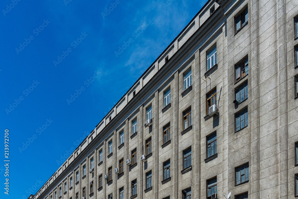 Old gray residential building of concrete and brick against the blue sky in summer