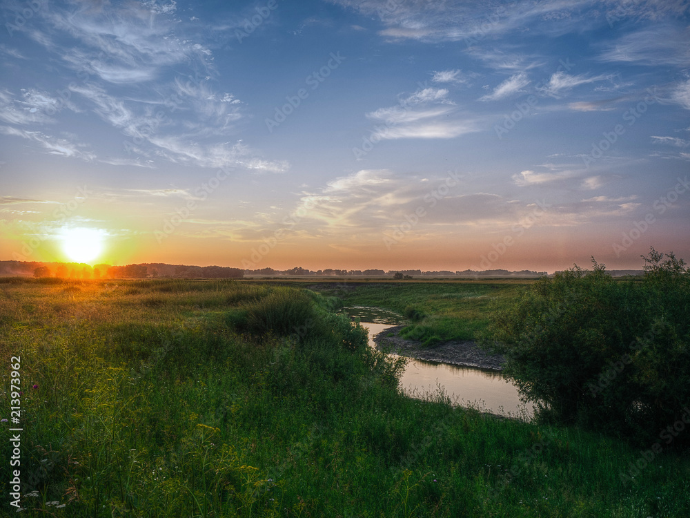 Beautiful view of a small curved river at sunset in summer. Landscape for the European part of Russia or Eastern Europe.