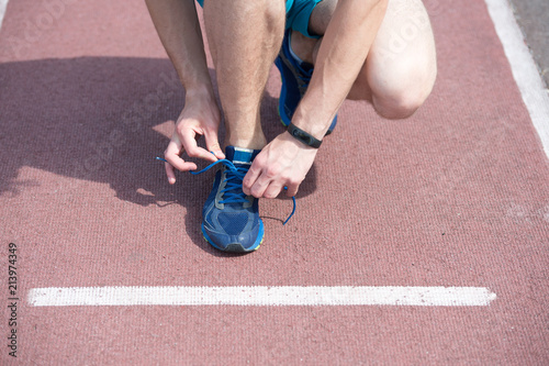 Shoes elite runners wearing marathon. Hands tying shoelaces on sneaker, running surface background. Hands of sportsman with pedometer tying shoelaces on sporty sneaker. Marathon equipment concept