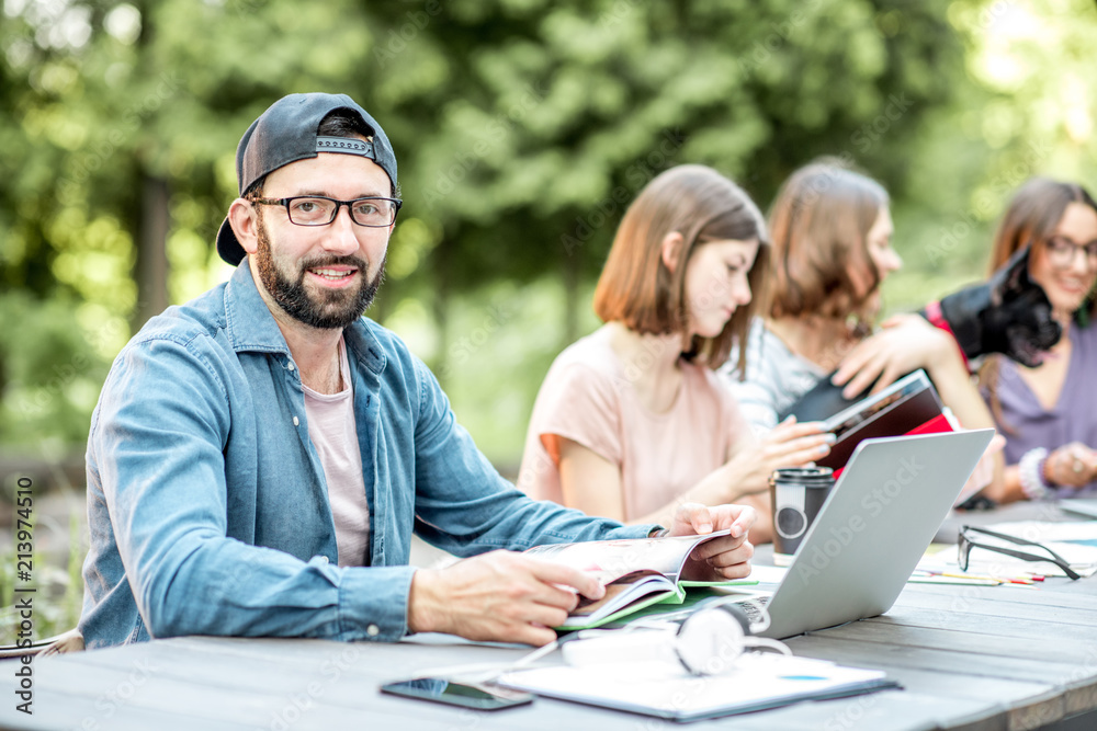 Young friends dressed casually studying with colorful books sitting at the table outdoors in the park Young friends dressed casually studying with colorful books sitting at the table outdoors in the park