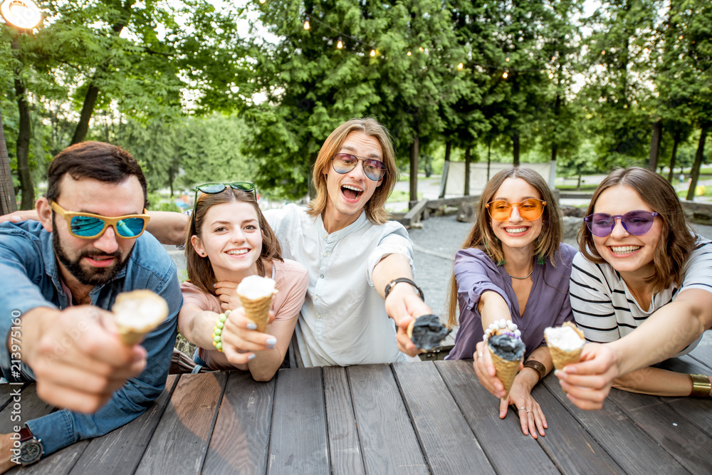 Obraz premium Young friends having fun with ice cream sitting together outdoors in the park