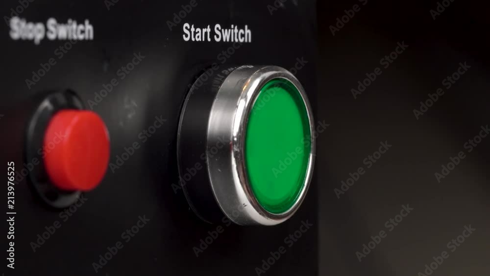 Closeup of two buttons in the frame. Green start switch and red stop switch buttons. Finger press the green start switch button.