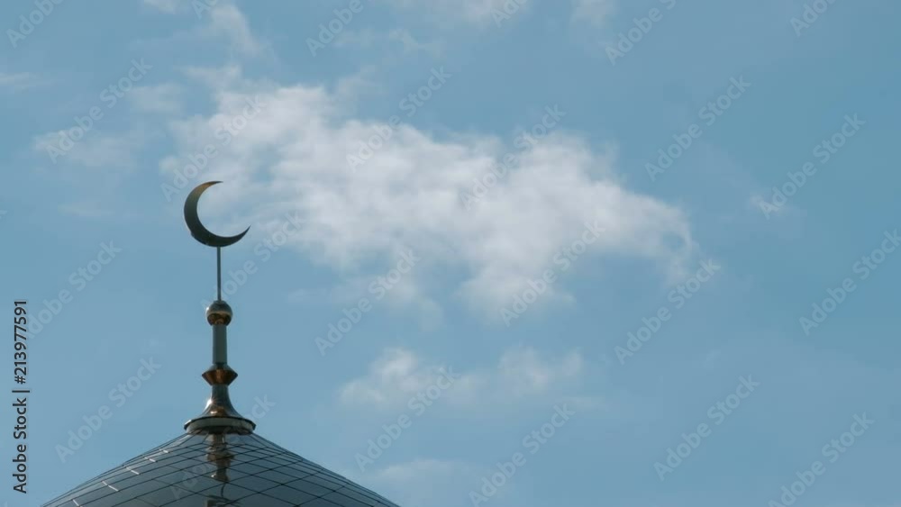 The clouds float past the golden crescent on the top of the mosque minaret. A symbol of the Muslim religion. A sunny day with a blue sky. The clouds float past the golden crescent on the top of the mosque minaret. A symbol of the Muslim religion. A sunny day with a blue sky.