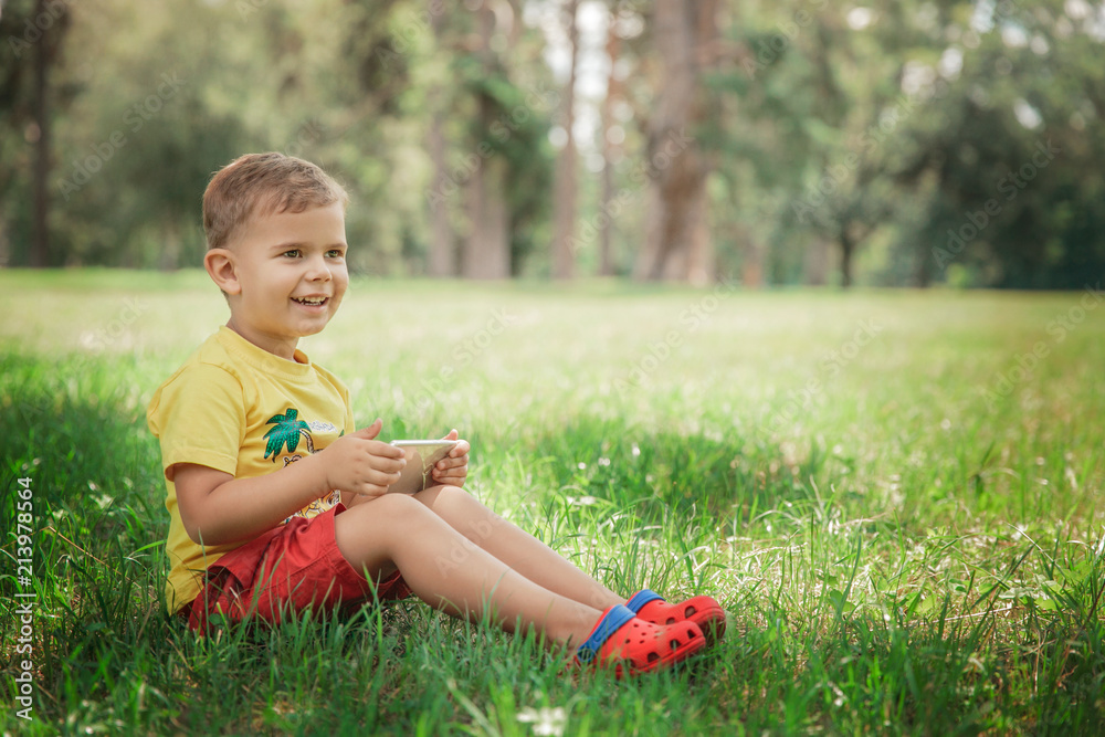 A little boy is sitting with the phone on the grass. A little boy is sitting with the phone on the grass.