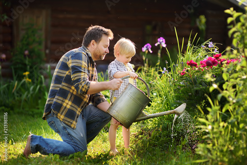 Middle age man and his little son watering flowers in the garden at summer sunny day
