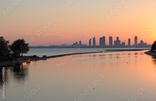Sun setting on Lake Ontario looking at a skyline of condos in Etobicoke from the shore in Toronto while a kayaker paddled in the far distance © shawn