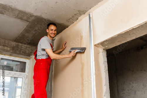A worker with spatula in workwear makes repairs the wall