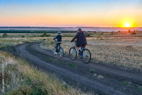 father and son ride a bike in the country on the field in the evening