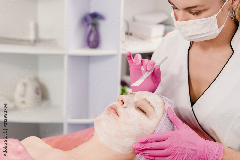 Female cosmetician doctor applying cream on face of young woman Female cosmetician doctor applying cream on face of young woman