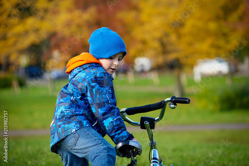 Cute european boy in the autumn city park. He is riding on his bicycle.