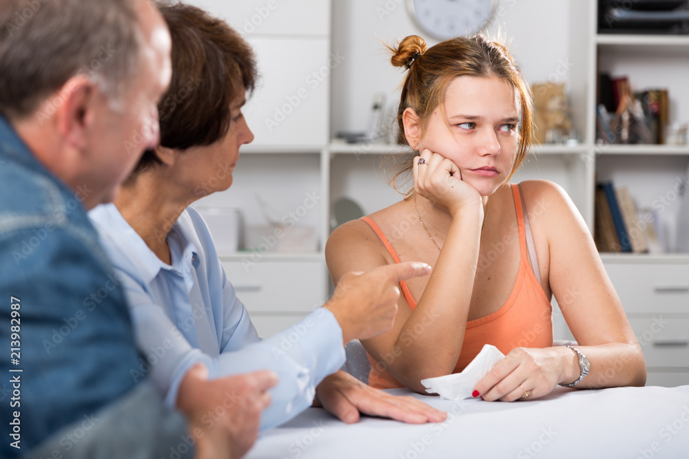 Fototapeta premium Adult couple is carefully talking with a sad daughter at the table