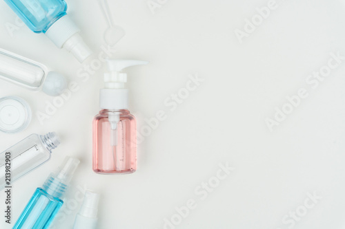 top view of the pink, blue and clear liquid containers with cream jar and make-up spatula on white background