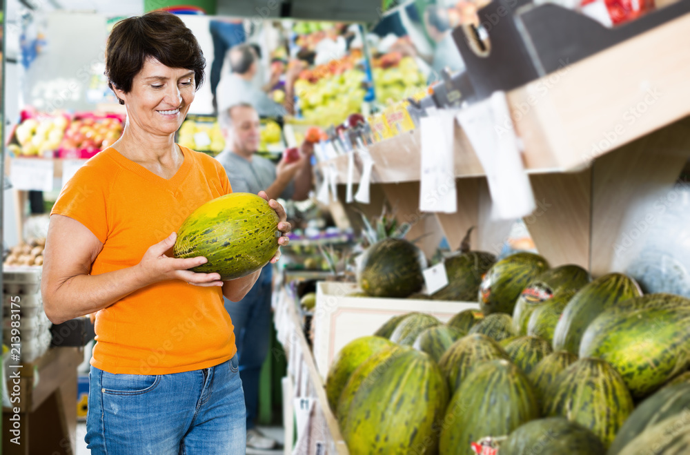 Fototapeta premium Smiling mature woman is choosing green melon
