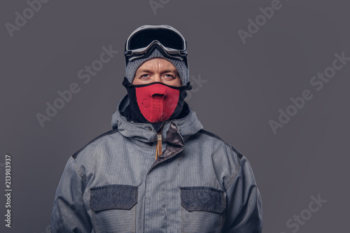 Portrait of a snowboarder dressed in a full protective gear for extream snowboarding posing at a studio. Isolated on a gray background.