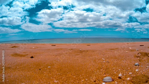 Beach sand with a small rocks and shells, calm waves splashing, clear blue sky 