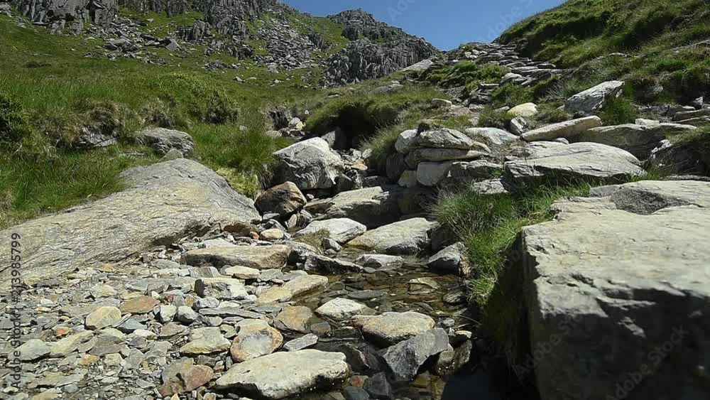 Water flowing over white rocks surrounded by grass covered mountains and rocky outcrops Water flowing over white rocks surrounded by grass covered mountains and rocky outcrops