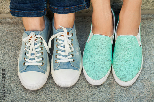 Close up view of two pairs girl s feet feet in blue sneakers