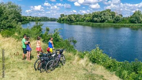 Family on bikes cycling outdoors, active parents and kids on bicycles, aerial view of happy family with children relaxing near beautiful river from above, sport and fitness concept 