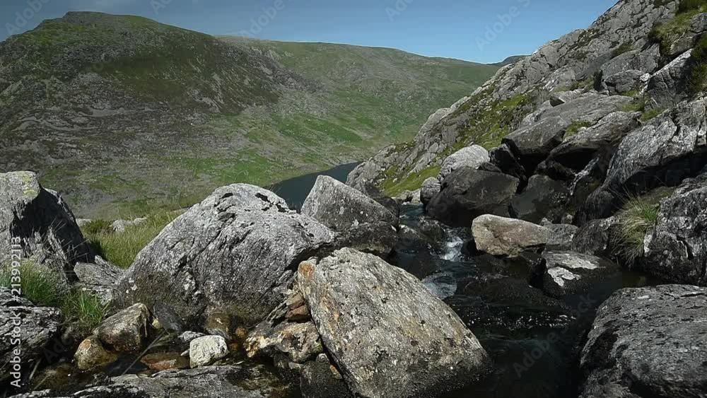 Water flowing over grey rocks with grass covered hills in the background Water flowing over grey rocks with grass covered hills in the background