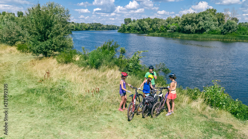 Family on bikes cycling outdoors, active parents and kids on bicycles, aerial view of happy family with children relaxing near beautiful river from above, sport and fitness concept 