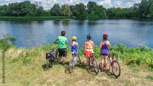 Family on bikes cycling outdoors, active parents and kids on bicycles, aerial view of happy family with children relaxing near beautiful river from above, sport and fitness concept 