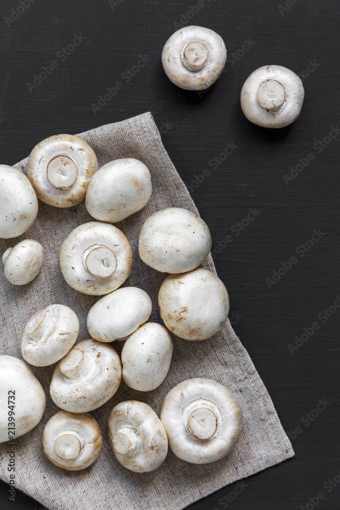 Champignon mushrooms on bamboo board over black background, top view. From above.