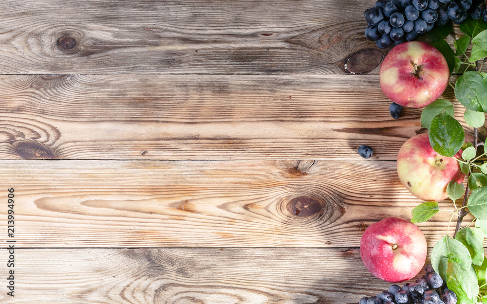 Ripe red apples with leaves and grapes on a wooden background. Autumn harvest. Top view. Copy space Ripe red apples with leaves and grapes on a wooden background. Autumn harvest. Top view. Copy space