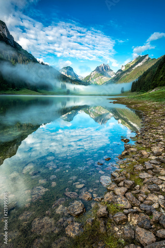 Reflection of mountains in the mountain lake with light fog over the valley