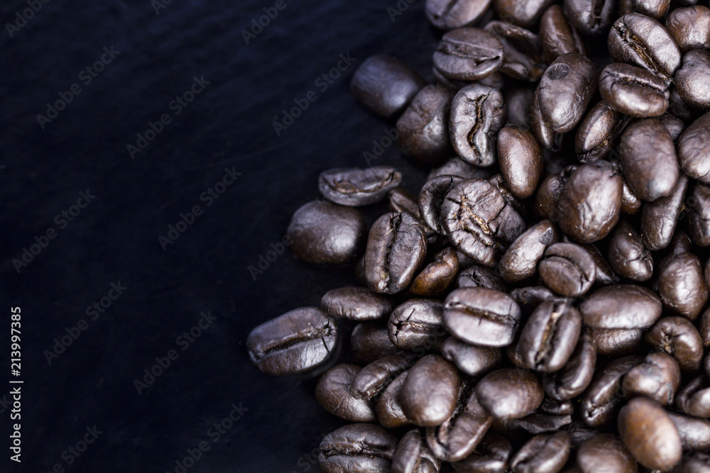 Naklejka premium Brown coffee beans on black surface. Top view close up.