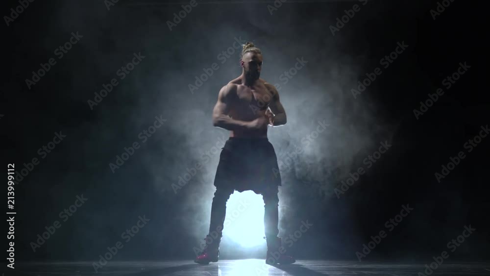 Pumped up guy dances sexy dance. Black smoke background