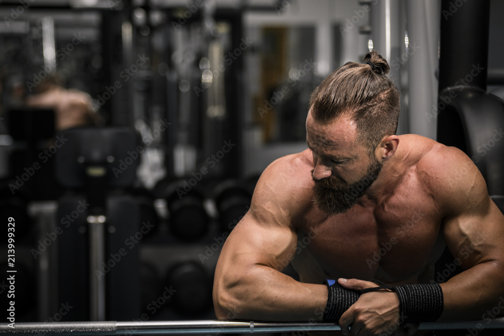 Hombre fuerte con grandes músculos descansando entre serie y serie mientras entrena en el gimnasio.