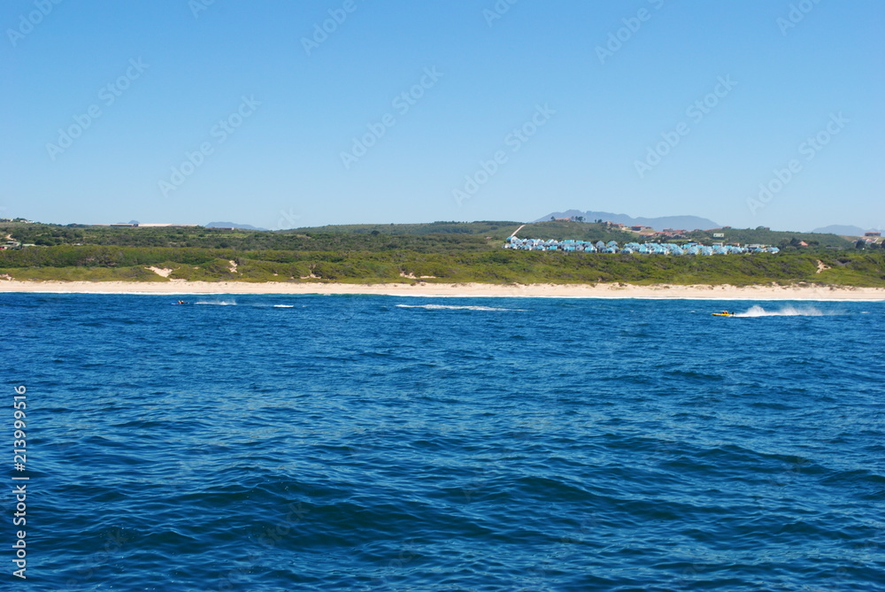 Ocean view of a line of houses with blue roofs sitting on the horizon above a beach in Mossel Bay, 2012