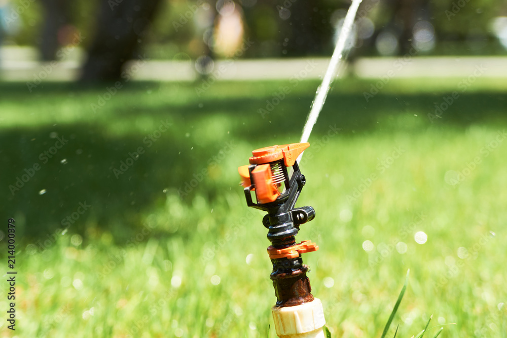 Sprinkler head watering the grass in the public park garden, close-up Sprinkler head watering the grass in the public park garden, close-up