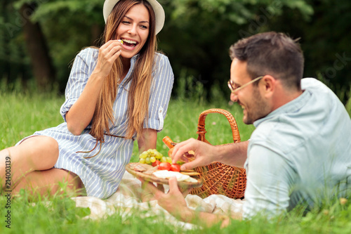 Beautiful happy young couple enjoying their time together, eating fruits and healthy food on picnic in a park. Love and dating, romance, lifestyle concept
