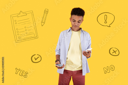 Choosing gadgets. Young smart boy holding two modern devices and thoughtfully looking at them while choosing the best one in a shop