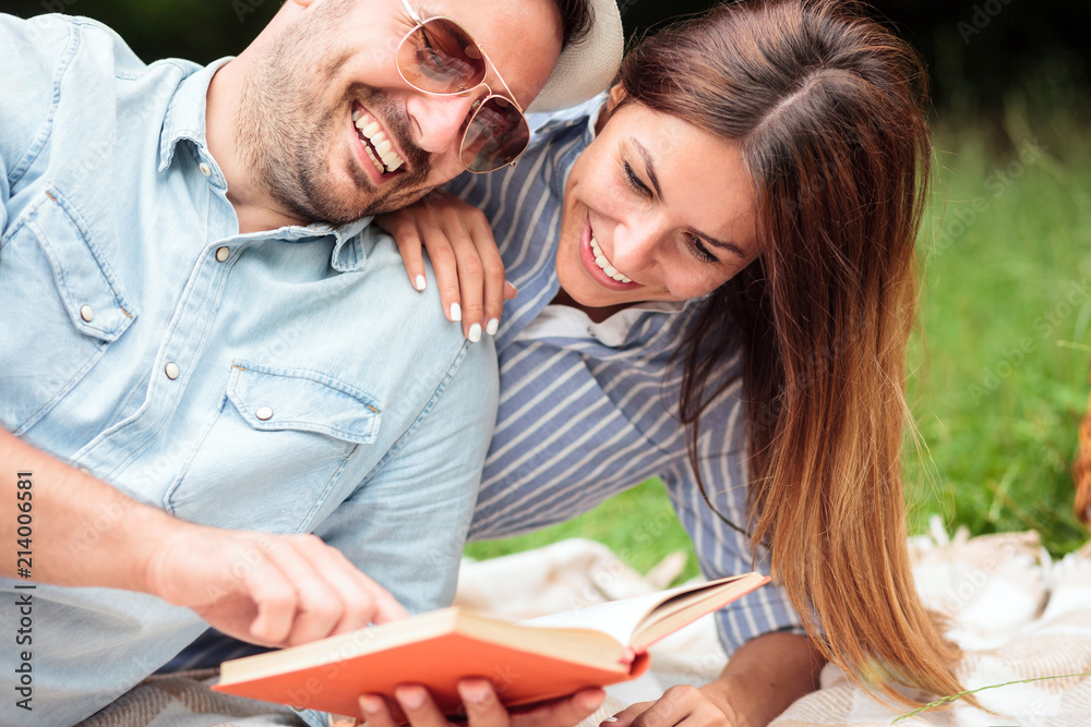 Beautiful young couple enjoying a good read during romantic picnic in a park. Lying next to each-other and laughing Love, dating, romance and lifestyle concept