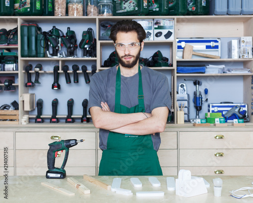 Portrait of a carpenter master with a beard in work clothes in a carpentry shop posing against a background of equipment