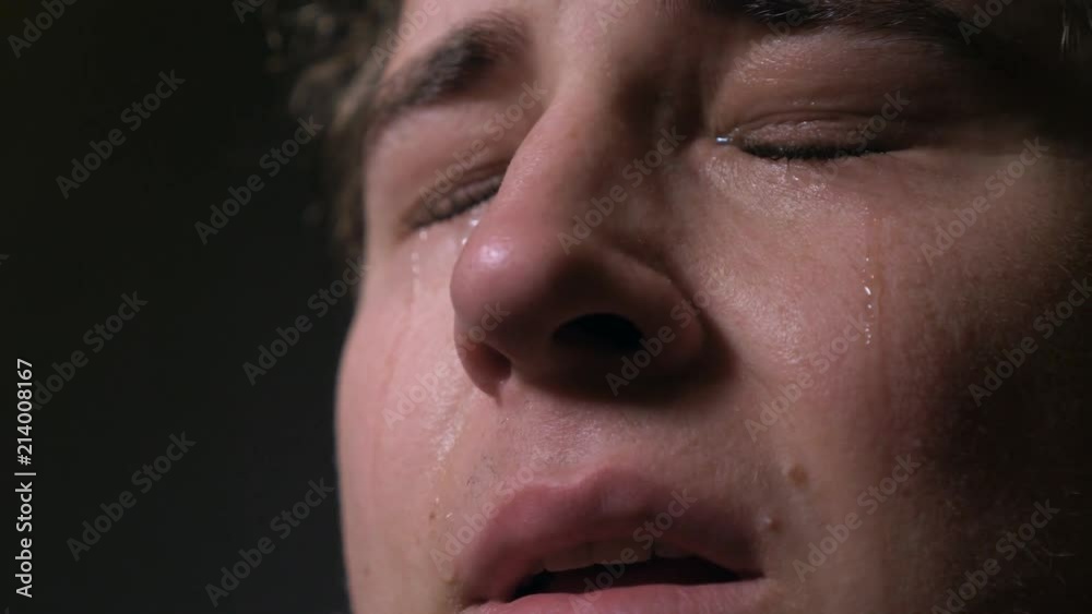 Crying sad young man in the dark looking up praying